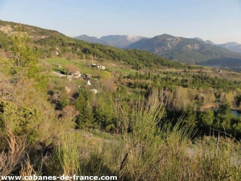 Cabanes en bois nichées dans la verdure, avec montagnes en arrière-plan.