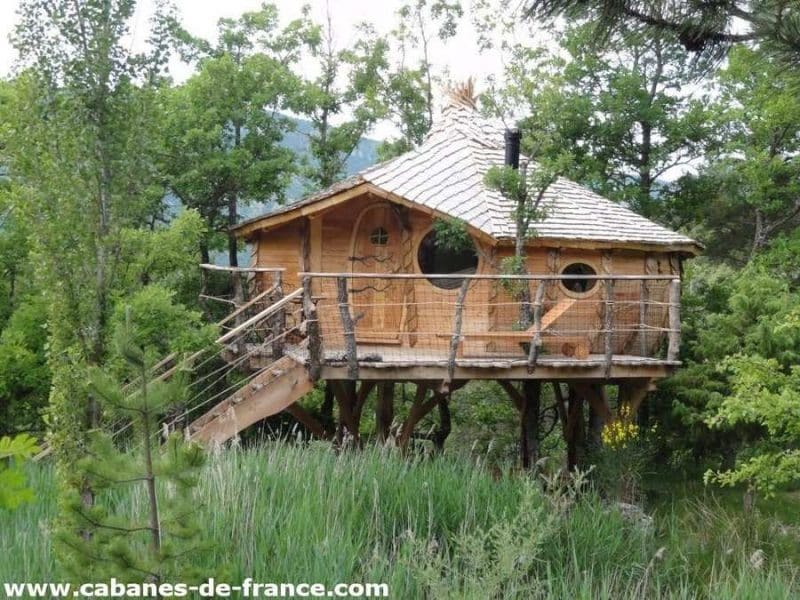 Cabane en bois perchée dans les arbres, entourée de verdure luxuriante.