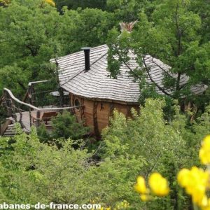 Cabane perchée en bois entourée de verdure, avec une terrasse en bois.
