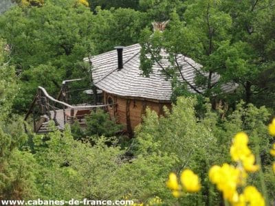 Cabane perchée en bois entourée de verdure, avec une terrasse en bois.