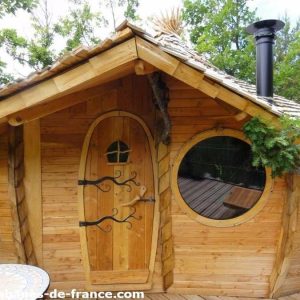 Cabane en bois avec un toit en ardoise et une grande fenêtre ronde, Auvergne-Rhône-Alpes.