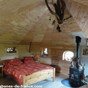 Cabane en bois cosy avec lit douillet et poêle à bois, ambiance chaleureuse.