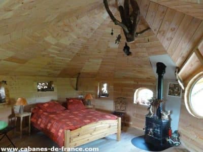 Cabane en bois cosy avec lit douillet et poêle à bois, ambiance chaleureuse.