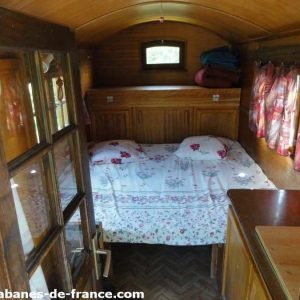 Intérieur dune roulotte en bois, lit douillet avec draps fleuris et fenêtres lumineuses.