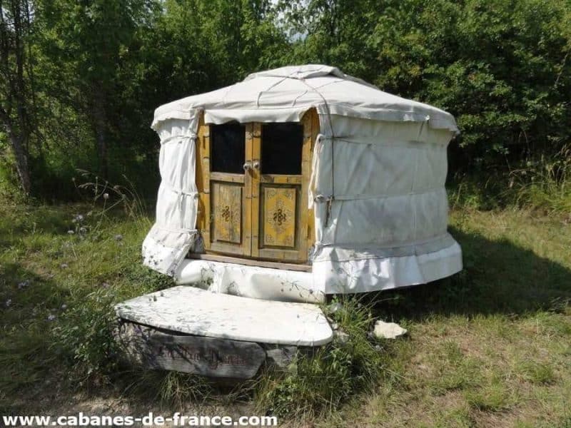 Yourte accueillante en pleine nature, avec une porte en bois décorée et un cadre verdoyant.