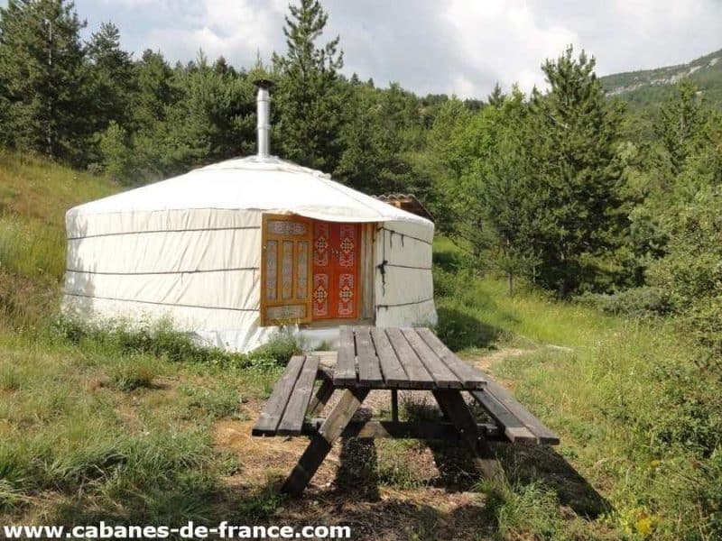 Yourte spacieuse en pleine nature, avec une table en bois à lextérieur.