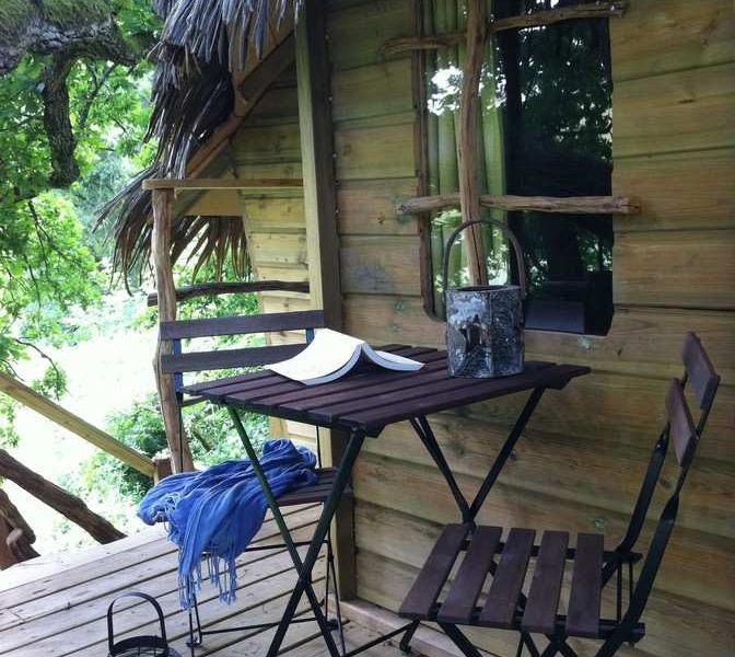 Cabane perchée en bois avec terrasse, vue sur la nature verdoyante.