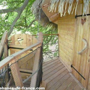 Cabane perchée en bois avec balustrade, entourée darbres verdoyants.