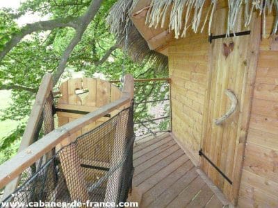 Cabane perchée en bois avec balustrade, entourée darbres verdoyants.