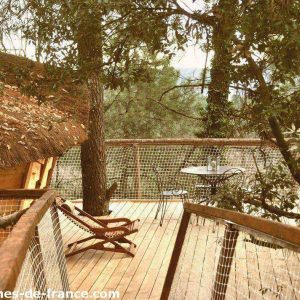 Cabane perchée en bois avec terrasse en bois, entourée darbres verdoyants.