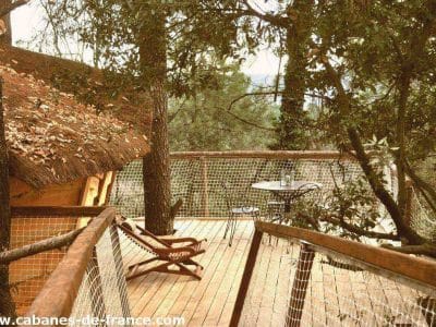 Cabane perchée en bois avec terrasse en bois, entourée darbres verdoyants.