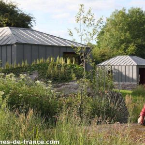 Cabane moderne en pleine nature, entourée de verdure et dun homme souriant.