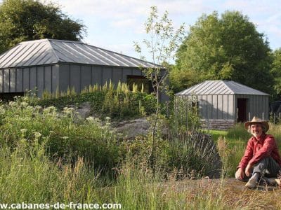 Cabane moderne en pleine nature, entourée de verdure et dun homme souriant.