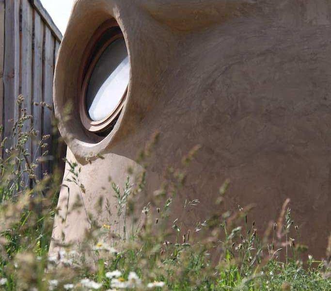Hébergement insolite en forme de bulle, avec une fenêtre ronde et un cadre naturel fleuri.