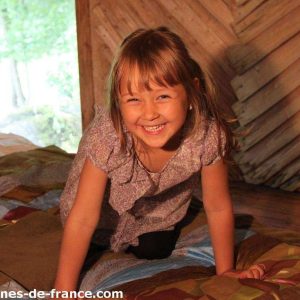 Cabane en bois dans les Pays de la Loire, avec une petite fille souriante sur un lit coloré.