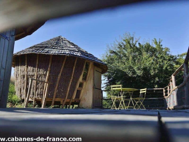 Hébergement insolite en cabane ronde, avec terrasse et chaises vertes.
