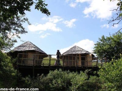 Cabane perchée dans les arbres, entourée de verdure et sous un ciel bleu.