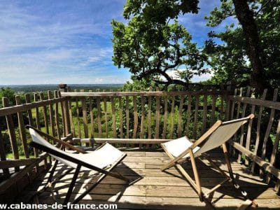 Cabane perchée en Midi-Pyrénées avec terrasse en bois et chaises confortables.