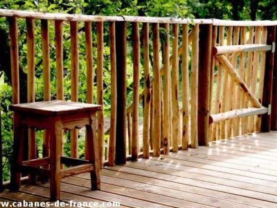 Cabane en bois en Aquitaine avec une terrasse en bois et un tabouret rustique.