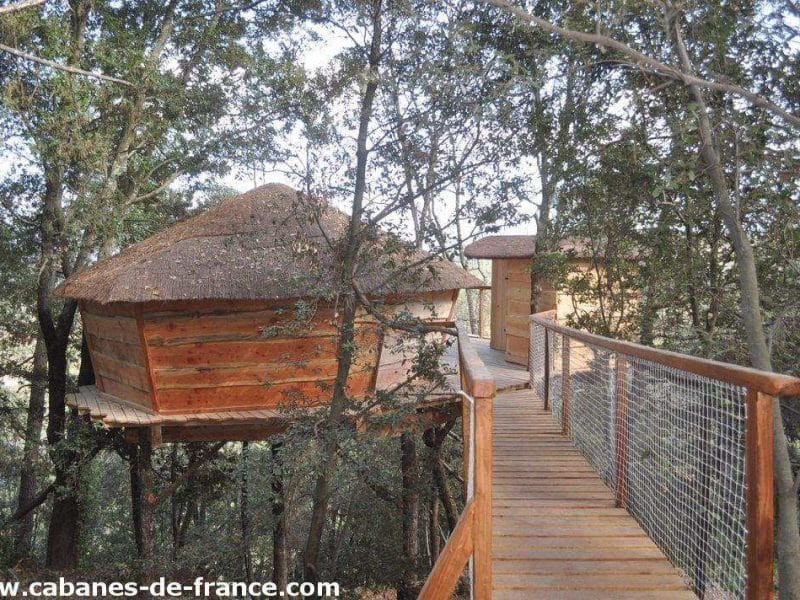 Cabane perchée en bois dans les arbres, accessible par un chemin en bois.