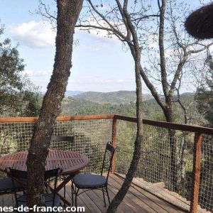 Cabane perchée en bois avec terrasse, vue panoramique sur la forêt en Auvergne-Rhône-Alpes.