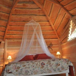 Cabane en bois avec un lit romantique sous un plafond en bois sculpté.