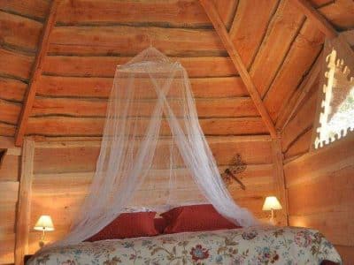 Cabane en bois avec un lit romantique sous un plafond en bois sculpté.