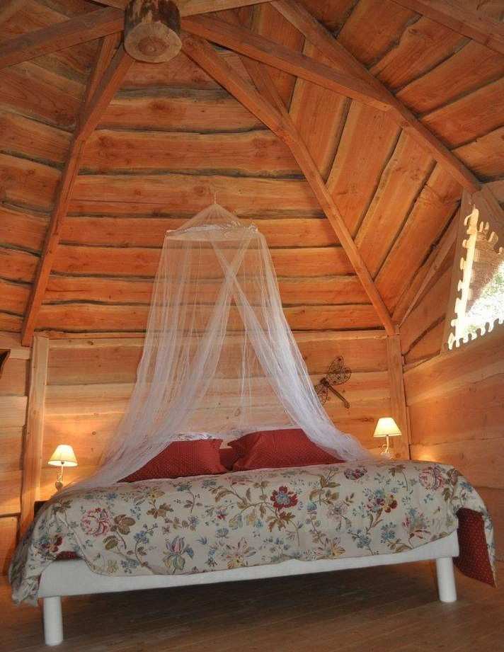 Cabane en bois avec un lit romantique sous un plafond en bois sculpté.