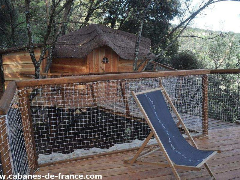 Cabane perchée en bois avec terrasse en bois et chaise longue, au cœur de la nature.