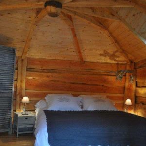 Chalet en bois chaleureux avec un lit douillet et un plafond en poutres apparentes.
