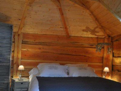 Chalet en bois chaleureux avec un lit douillet et un plafond en poutres apparentes.