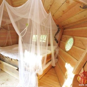 Cabane en bois avec lit entouré dun voile, ambiance chaleureuse et naturelle.