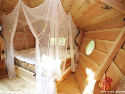 Cabane en bois avec lit entouré dun voile, ambiance chaleureuse et naturelle.