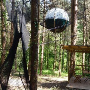 Hébergement insolite en Aquitaine : cabane suspendue avec sphère en filet dans les arbres.