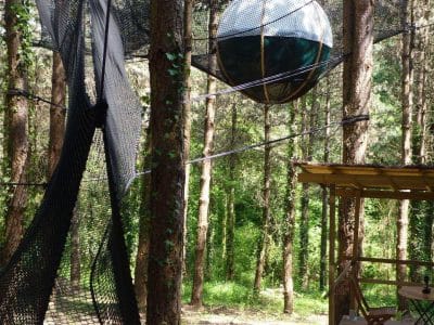 Hébergement insolite en Aquitaine : cabane suspendue avec sphère en filet dans les arbres.