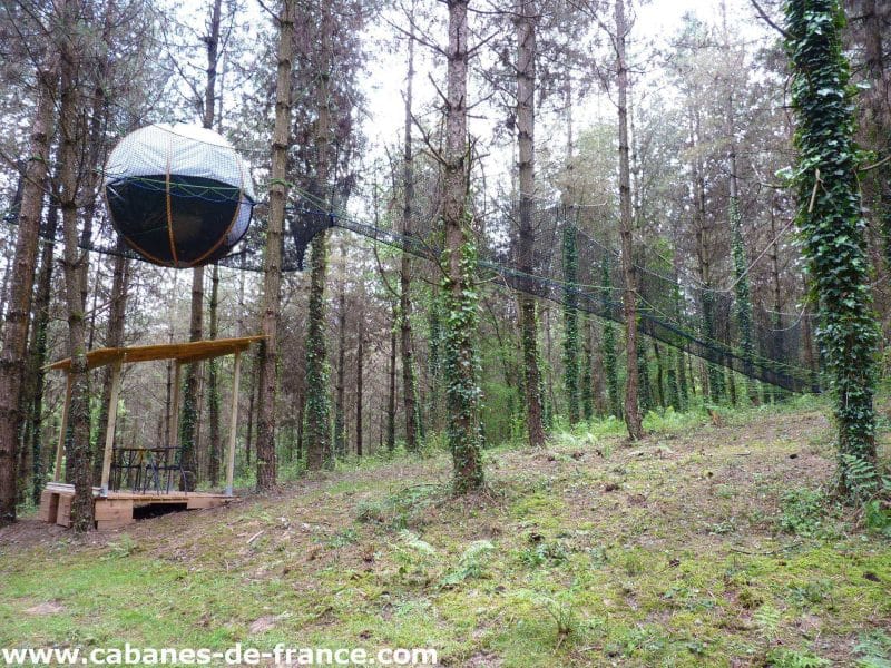 Cabane suspendue dans les arbres, entourée de pins verdoyants en Aquitaine.