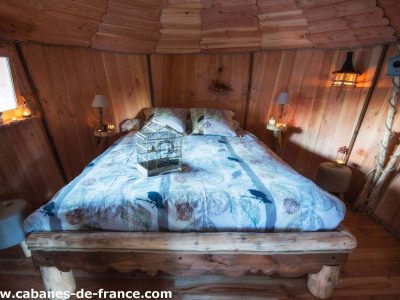 Cabane en bois à Grand-Est, lit douillet entouré de lanternes chaleureuses.