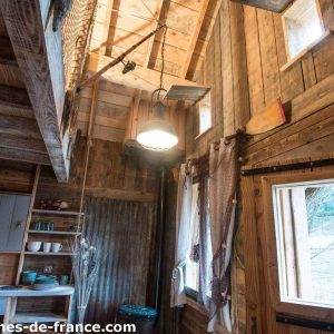 Cabane en bois dans les arbres, intérieur chaleureux avec lumière suspendue.