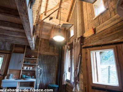 Cabane en bois dans les arbres, intérieur chaleureux avec lumière suspendue.