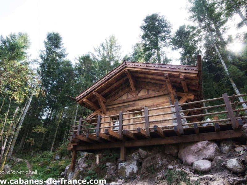 Cabane en bois perchée, entourée de verdure, offrant une vue imprenable sur la forêt.