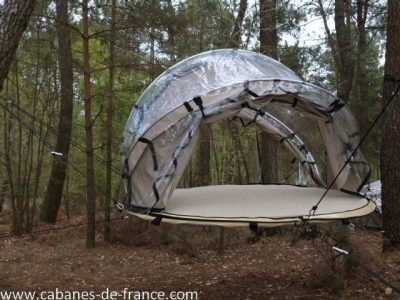 Hébergement insolite en Bretagne : tente suspendue transparente dans les arbres.