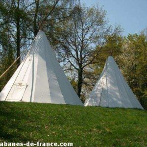 Tentes tipi blanches en pleine nature, entourées darbres verdoyants en Auvergne.