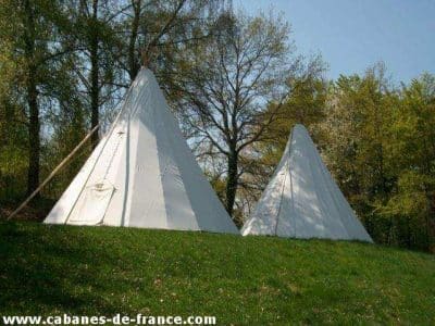 Tentes tipi blanches en pleine nature, entourées darbres verdoyants en Auvergne.