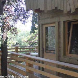 Cabane perchée en bois avec balcon, entourée de verdure à Languedoc-Roussillon.