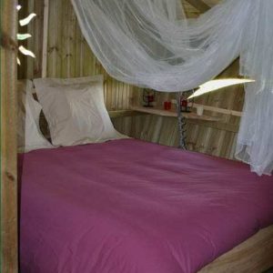 Cabane en bois en Bourgogne, lit douillet avec drap rose et voilages légers.