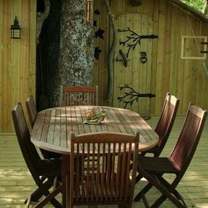 Cabane en bois dans un arbre, avec une terrasse et une table en bois accueillante.
