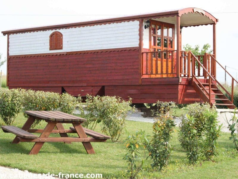 Charmante roulotte en bois rouge avec terrasse, entourée de verdure.