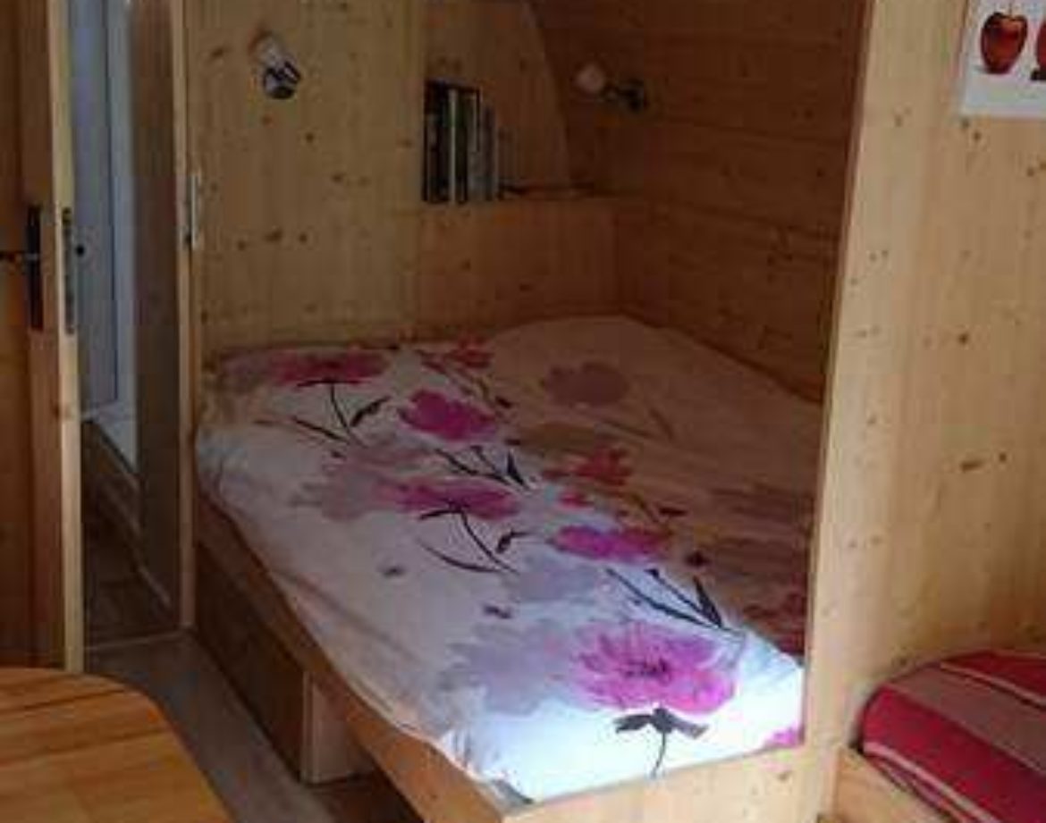 Cabane en bois cosy avec lit douillet et décor floral, idéale pour un séjour unique.