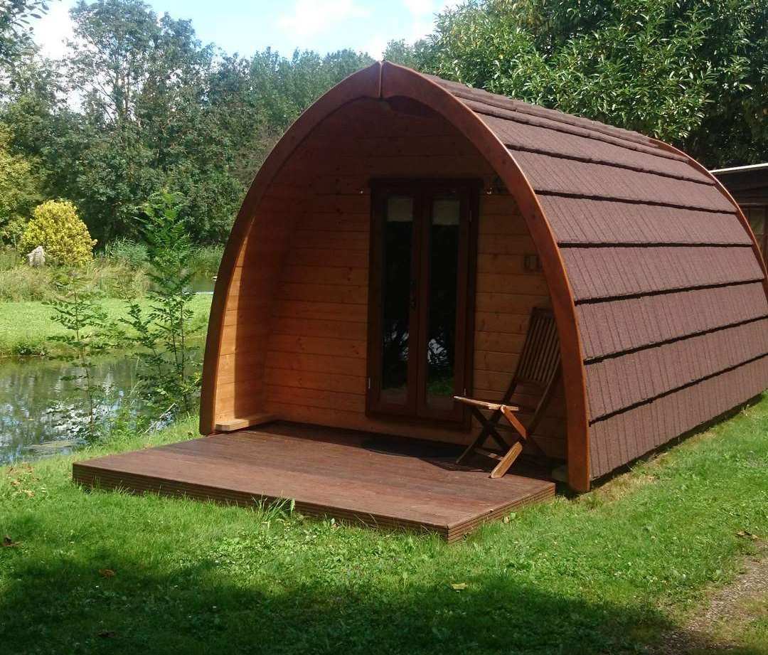 Cabane en bois au bord de leau, avec une terrasse ensoleillée et un cadre verdoyant.