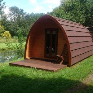 Cabane en bois au bord de leau, avec une terrasse ensoleillée et un cadre verdoyant.